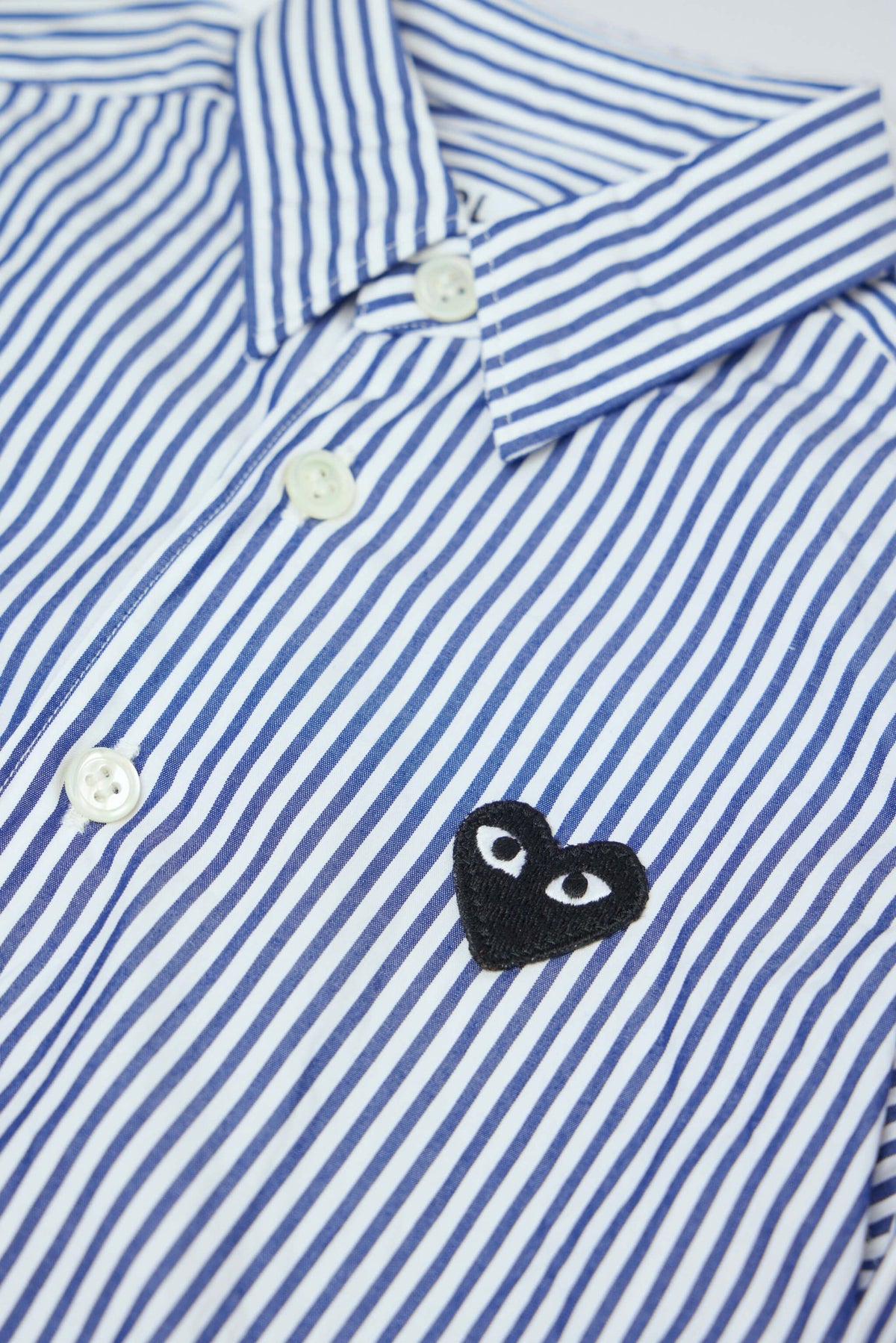 Close-up of Comme des Garçons PLAY heart emblem on black cotton shirt