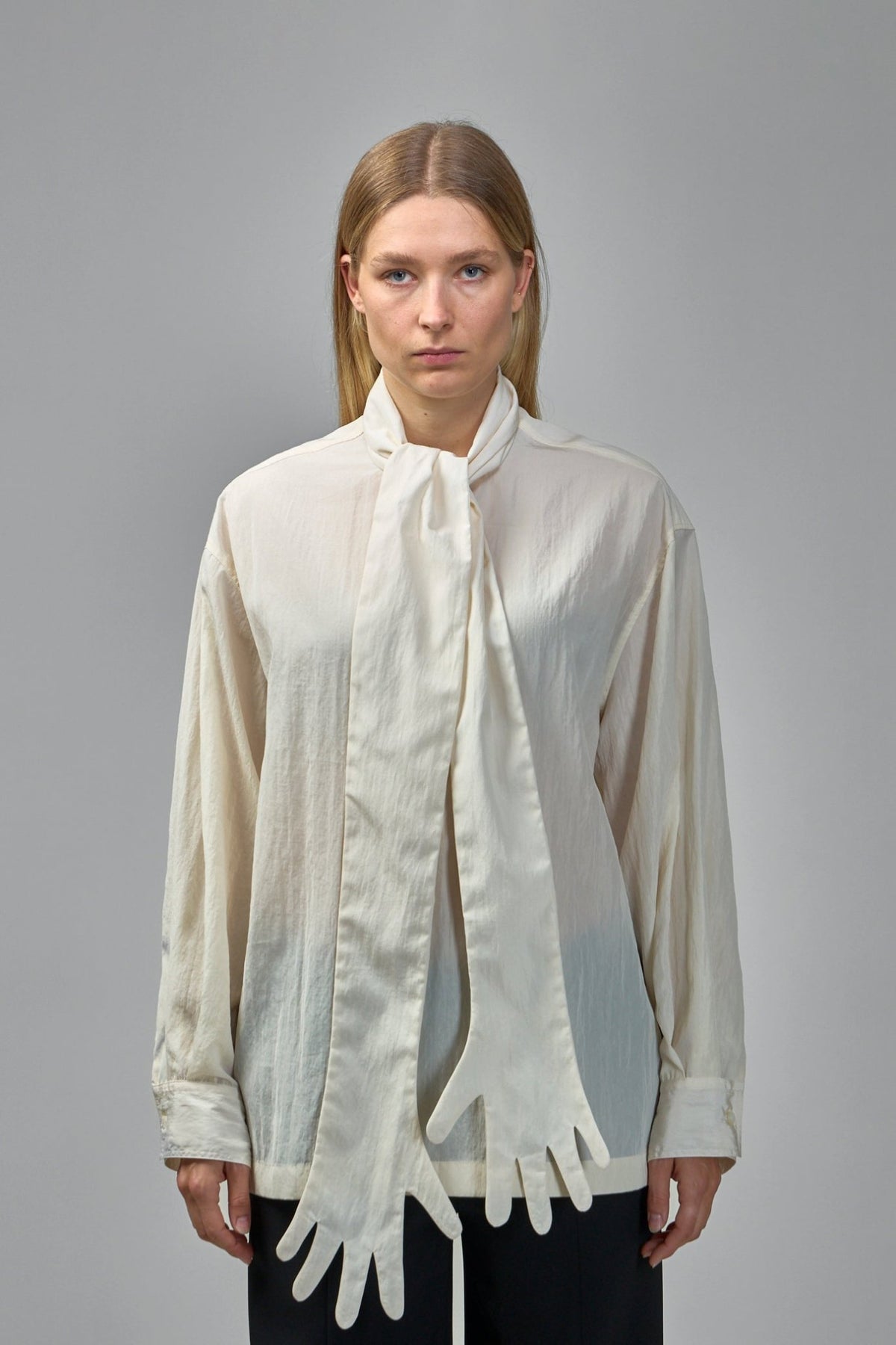 Close-up of glove-shaped scarf ends detail on cream oversized blouse