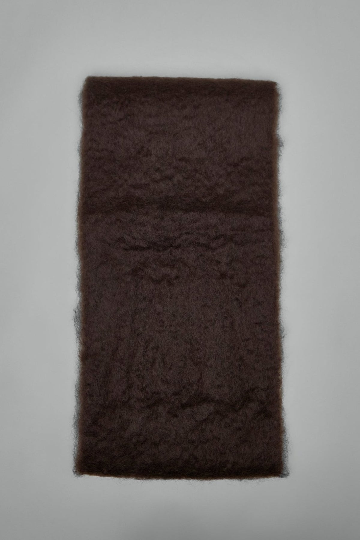 Close-up of white Jil Sander logo patch on dark brown fluffy scarf