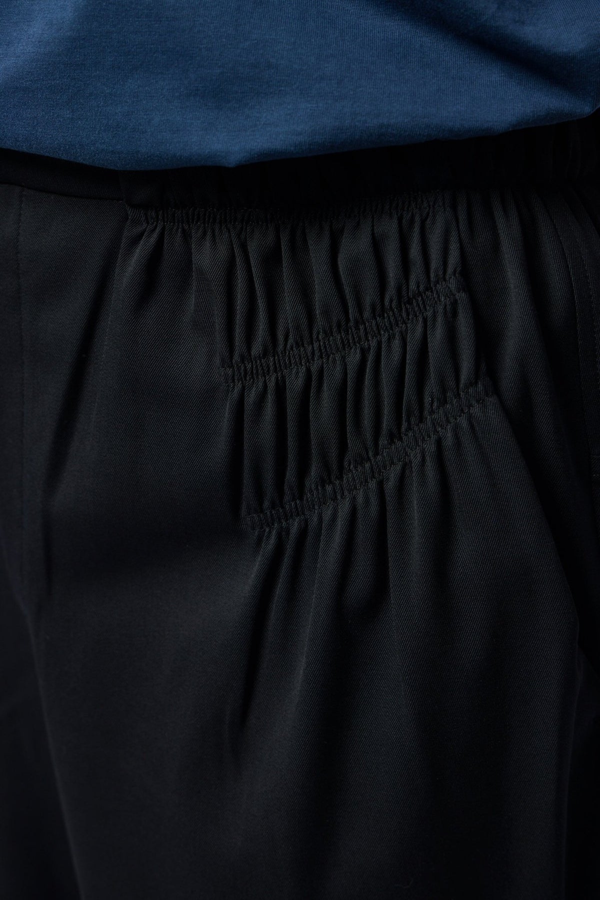 Model wearing black gathered trousers with minimalist styling